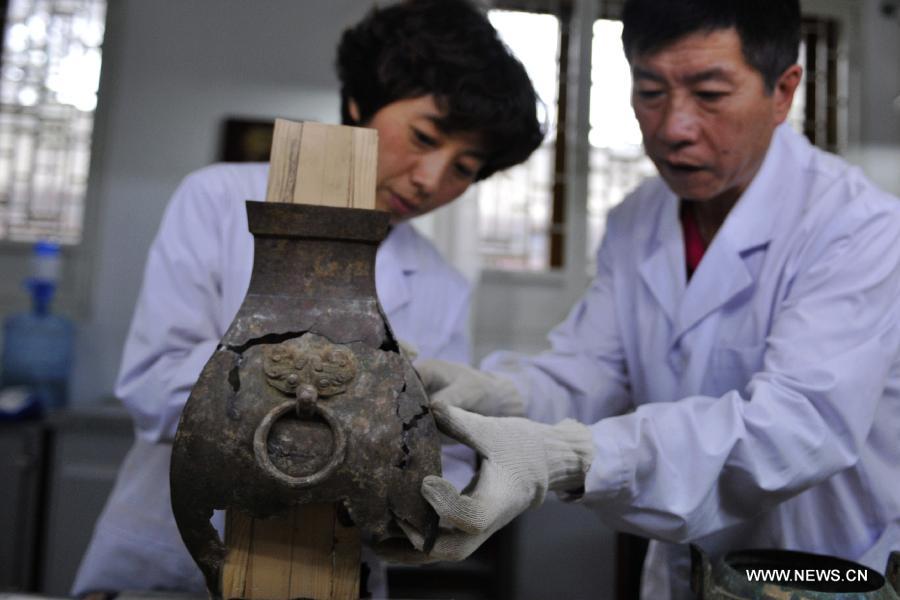 Li Xiaolong (R), an expert on cultural relics preservation, discusses with his colleague on how to repair a bronze ware at the relics conservation center of the museum of Tianshui City, northwest China's Gansu Province, July 15, 2013. A total of six cultural relics preservation experts of the museum conduct the conservation work on relic items here. They use modern technology as well as traditional handicraft to repair and restore cultural relic fragments and damaged bronze wares. (Xinhua/Chen Bin) 