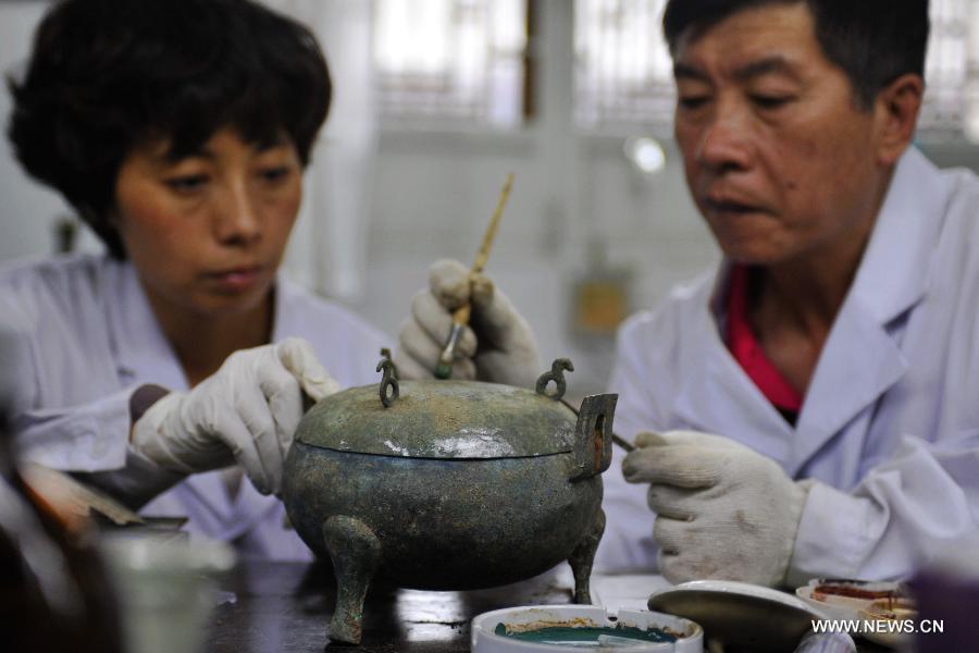 Li Xiaolong (R), an expert on cultural relics preservation, colors a bronze ware with his colleague at the relics conservation center of the museum of Tianshui City, northwest China's Gansu Province, July 15, 2013. A total of six cultural relics preservation experts of the museum conduct the conservation work on relic items here. They use modern technology as well as traditional handicraft to repair and restore cultural relic fragments and damaged bronze wares. (Xinhua/Chen Bin)