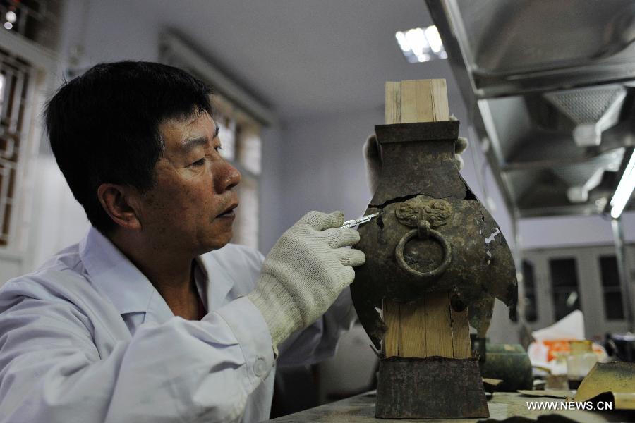 Li Xiaolong, an expert on cultural relics preservation, checks the damages on a bronze ware from the Han Dynasty (202 BC - 221 AD) at the relics conservation center of the museum of Tianshui City, northwest China's Gansu Province, July 15, 2013. A total of six cultural relics preservation experts of the museum conduct the conservation work on relic items here. They use modern technology as well as traditional handicraft to repair and restore cultural relic fragments and damaged bronze wares. (Xinhua/Chen Bin) 