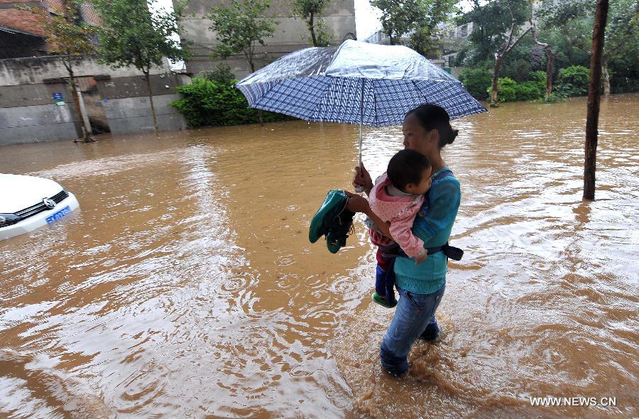 A woman hugging her child walks in the flood water in Kunming, capital of southwest China's Yunnan Province, July 19, 2013. Kunming was hit by a heavy rainstorm from Thursday to Friday. (Xinhua/Lin Yiguang)