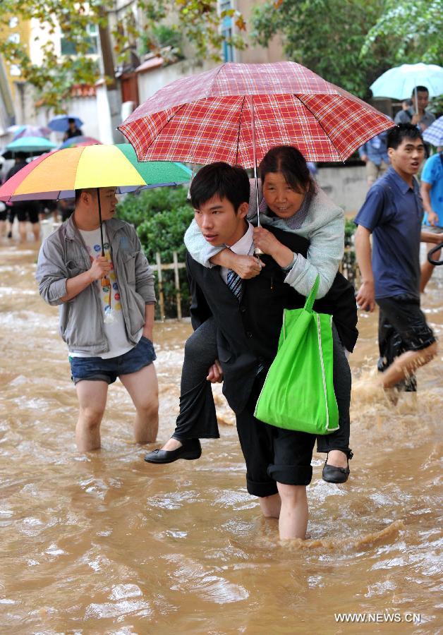 A man carrying an elder citizen walks past the flooded Jinbi Road in Kunming, capital of southwest China's Yunnan Province, July 19, 2013. Kunming was hit by a heavy rainstorm from Thursday to Friday. Kunming's meteorologic center on Friday issued a blue alert for rainstorm. (Xinhua/Lin Yiguang)