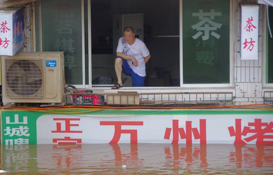 A man watches flood from the window at the second floor of a building on Binhe Road in Quxian County of Dazhou City, southwest China's Sichuan Province, July 20, 2013. Due to sustained heavy rainfall, this year's highest flood peak of the Qujiang River which runs through northeast Sichuan and west Chongqing, a southwest China's municipality near Sichuan, passed Quxian County Saturday. More than one third of the downtown area of Quxian County was flooded. (Xinhua/Yu Junhua)