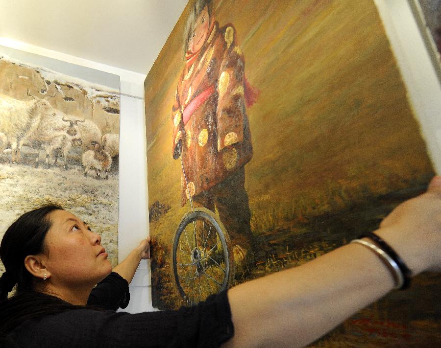 Woman painter Zhou Hua puts up a painting work at her art gallery on Barkhor Street of Lhasa, capital of southwest China's Tibet Autonomous Region on July 18, 2013. Having lived in Lhasa since she was very young, Zhou Hua speaks Tibetan fluently and has great affection to her Tibetan fellows. She has opened the art gallery for over 10 years with thousands of painting works depicting portraits of Tibetans. Experiencing Tibet and its people with love and life, 34-year-old Zhou Hua becomes a woman painter with unique style in the art circle of Tibet. [Photo/Xinhua]