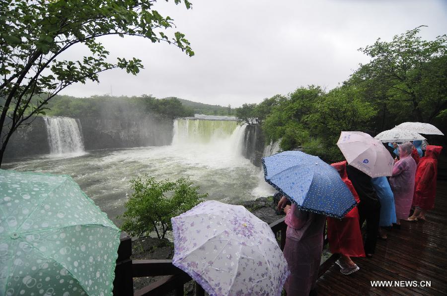 Tourists enjoy the scenery against rain in front of the Diaoshuilou Waterfall at the Jingpo Lake in Mudanjiang City, northeast China's Heilongjiang Province, July 21, 2013. The water level of the Jingpo Lake rose significantly due to the continuous rainfalls upstream. (Xinhua/Zhang Chunxiang)
