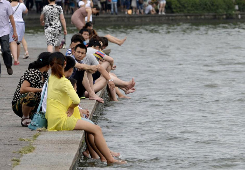 Tourists in Hangzhou, Zhejiang province take off their shoes and dip their feet into the West Lake to cool off. (Chinanews.com)