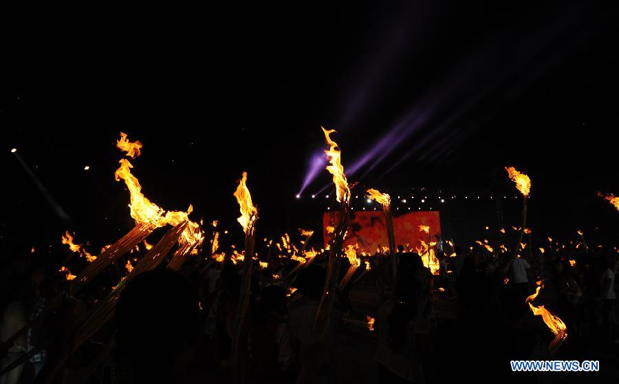 Tourists hold burning torches to celebrate the Torch Festival at Yunnan Nationalities Village in Kunming City, southwest China's Yunnan Province, July 28, 2013. The Torch Festival, which falls around the 24th day of the sixth Chinese lunar month every year, is the traditional holiday of the Yi ethnic group and some other ethnic groups. (Xinhua/Qin Lang)