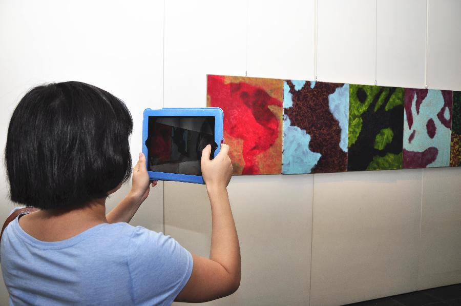 A visitor takes pictures of art works at the exhibition "The Strength of Natural Impulses" in Beijing, capital of China, July 30, 2013. Jointly contributed by French artist Francois Bossiere and four Chinese artists Zhang Sen, Zhang Yuqing, Sun Qianwei and Xie Hong, the exhibition concerned with visual art will be held from July 30 to Aug. 6 in Beijing. (Xinhua/Wang Jingqiang) 