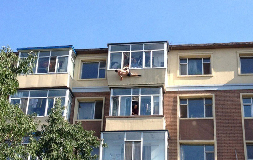A man tries to jump from the building to commit suicide in a residential area in Changchun, captial of China's Jilin Province, July 31, 2013. While he jumped out of the window, his leg was caught by his wife. Later he was rescued by the neighbors and policemen. (Photo/Xinhua)