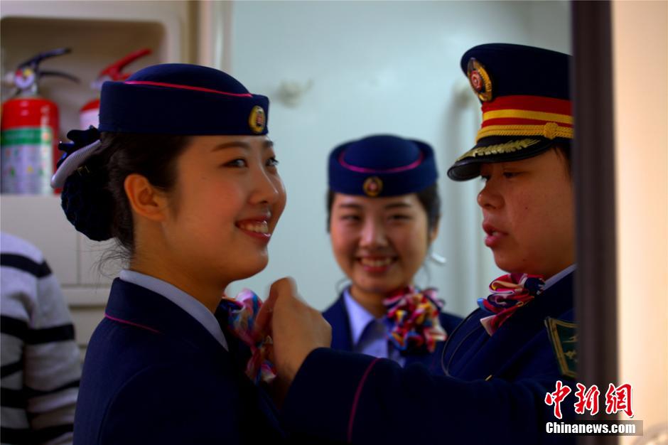 Chief attendant Su Hong helps Yan Huan and Yan Yi trim their uniforms on the train T58. (Chinanews.com/Hu Zhiqiang)